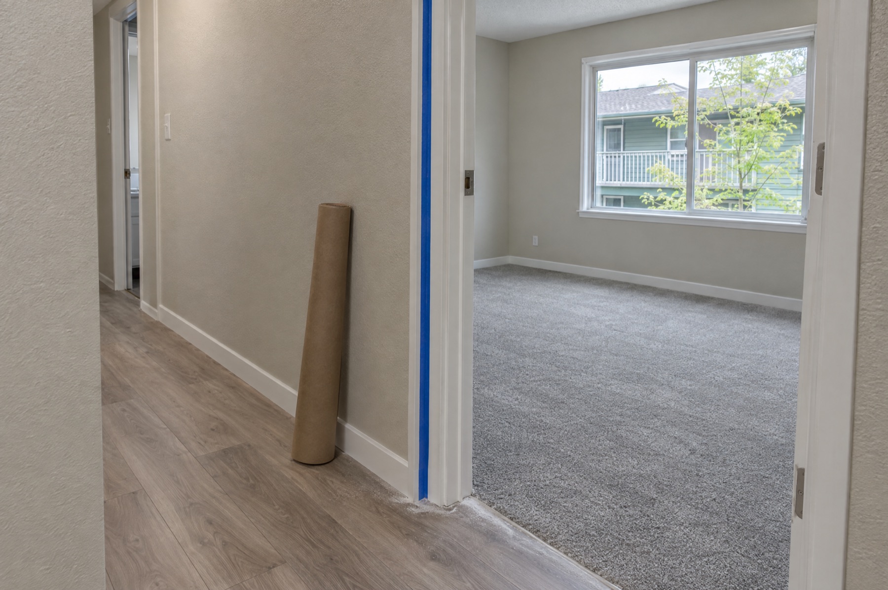 Hallway of a freshly renovated apartment with new plank flooring, painter's tape on the door casing and dust along the baseboard