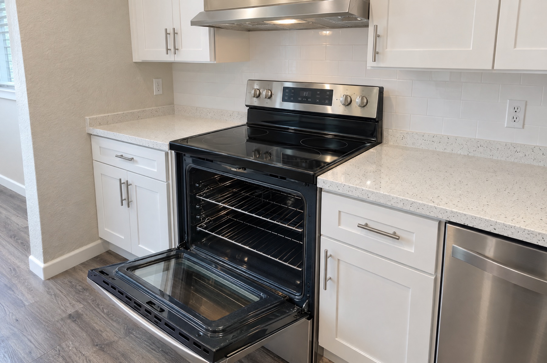 Galley kitchen with white shaker cabinets and a stainless range with the oven door open