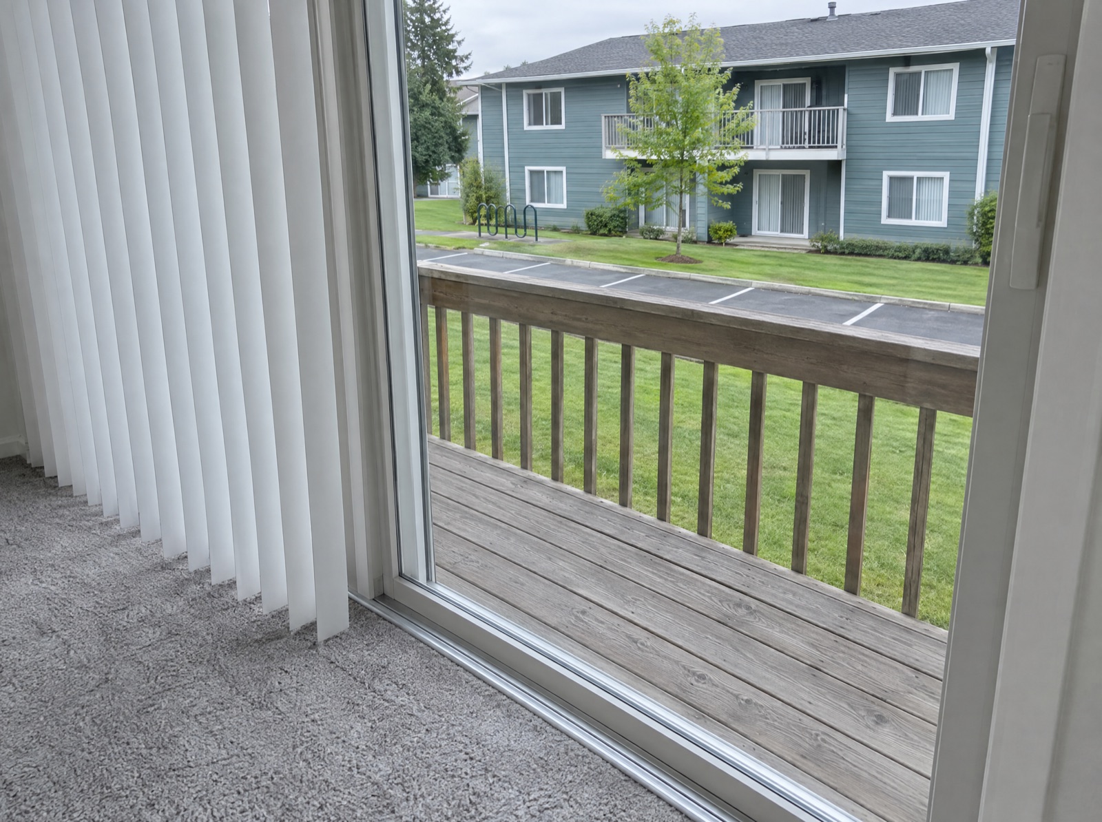 Sliding glass door track and white vertical blinds, with the neighboring building, lawn and parking outside